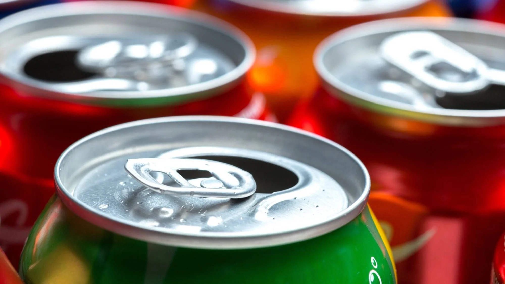 Varias latas de aluminio de bebidas gaseosas en colores verde y rojo, con una abierta en primer plano.