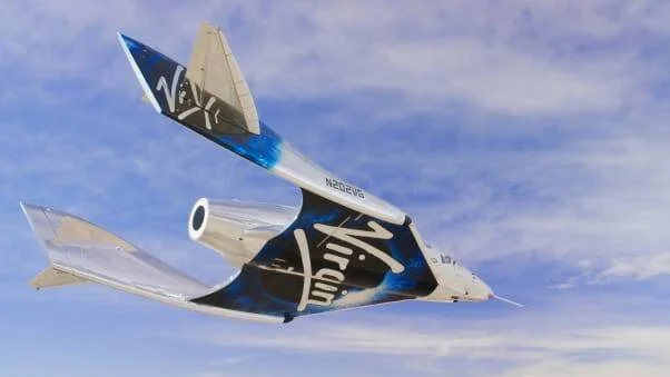 Nave suborbital de Virgin Galactic volando con cielo azul de fondo, mostrando su diseño aerodinámico con cola en V.