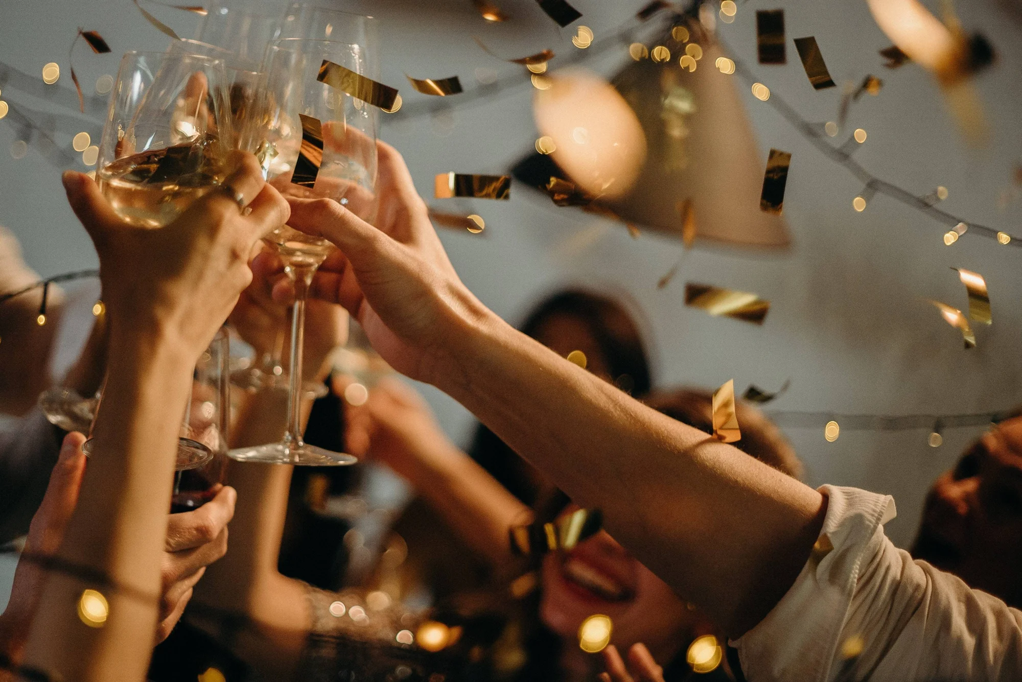 Grupo de personas alzando copas de champán en un brindis celebratorio mientras cae confeti dorado.