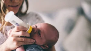 Una mujer sostiene a un bebé recién nacido y le da el biberón con leche.