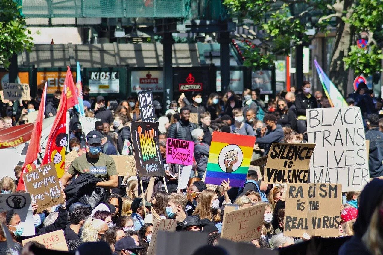 Multitud en protesta callejera sosteniendo carteles contra el racismo y en defensa de los derechos trans y negros.