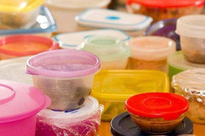 Múltiples envases de plástico de colores con tapas apilados sobre una superficie, usados para almacenar alimentos.