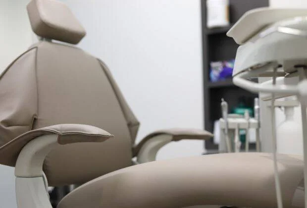Sillón odontológico tapizado en beige con instrumental dental al fondo en un consultorio.