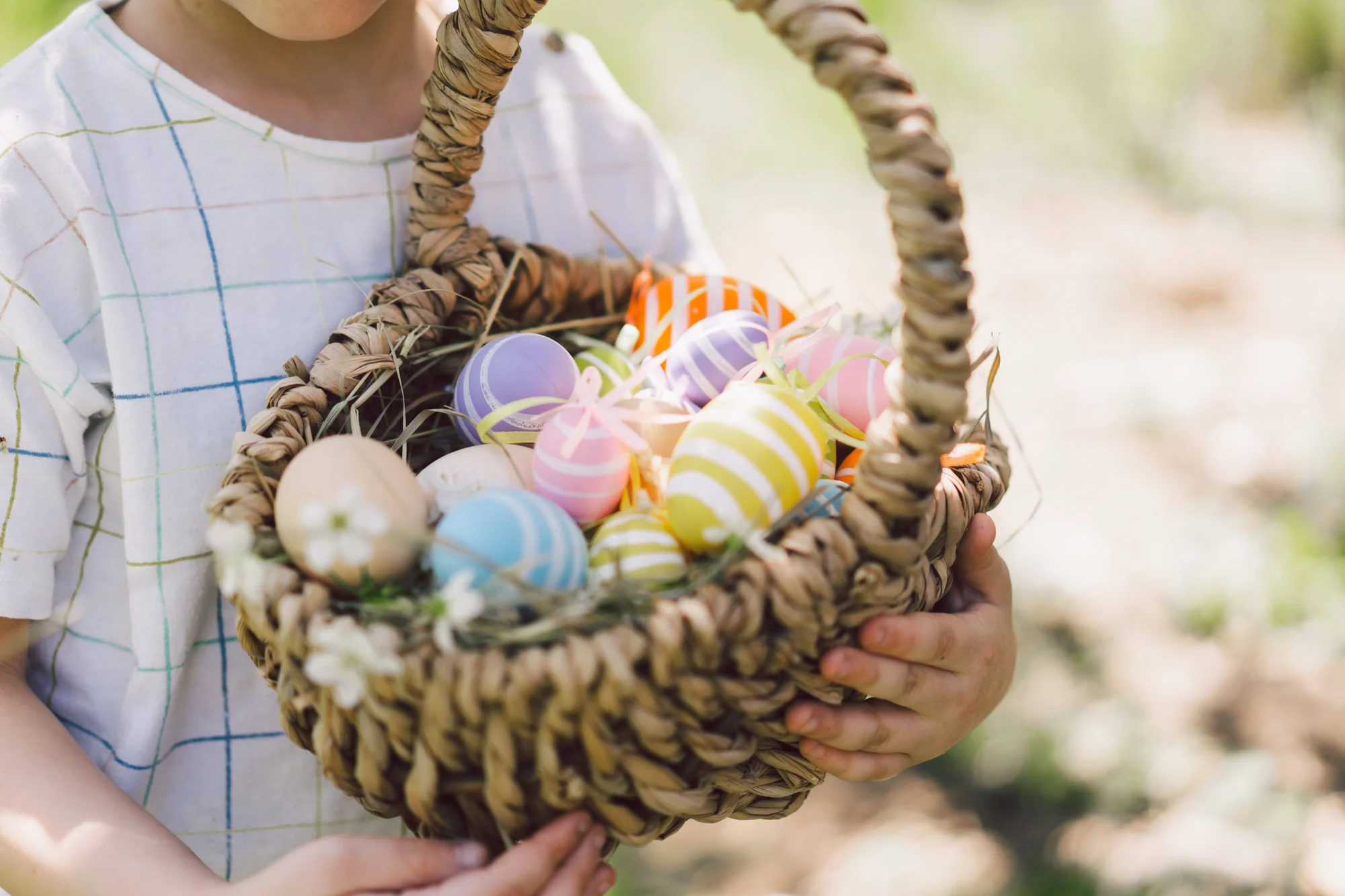 Un niño sostiene una canasta de mimbre llena de huevos de Pascua de colores pastel decorados con rayas.