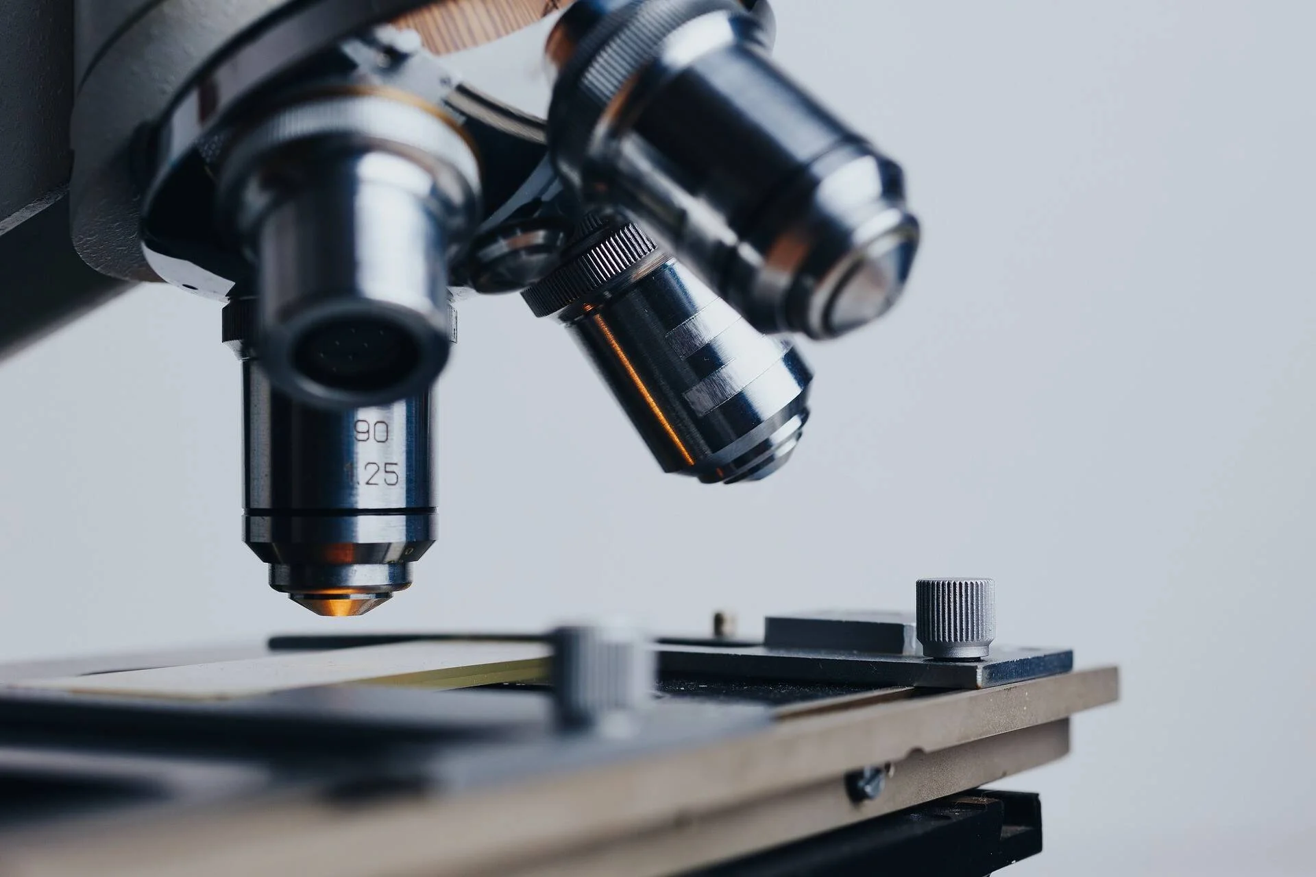 Primer plano de los objetivos metálicos de un microscopio óptico sobre una platina con portaobjetos.