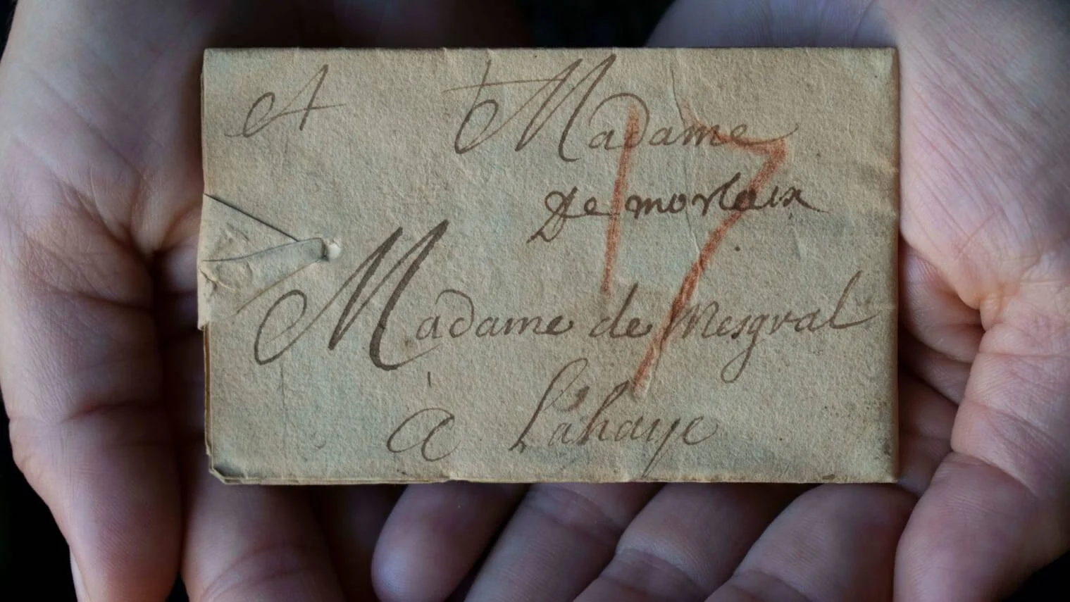 Mano sosteniendo una carta histórica manuscrita en francés dirigida a 'Madame de Mesgval à Lahaye'.