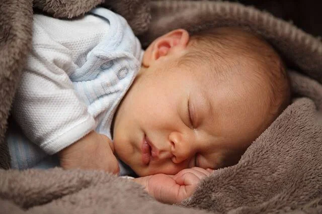Bebé recién nacido dormido plácidamente, envuelto en una manta gris suave.