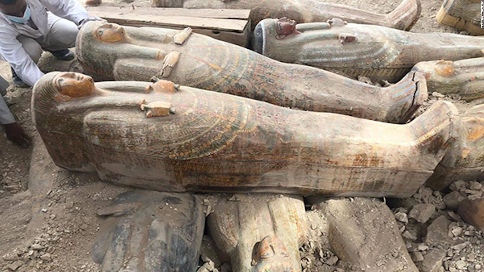 Varios sarcófagos antropomorfos de madera pintada del antiguo Egipto recién excavados, con decoraciones policromadas y rostros esculpidos.