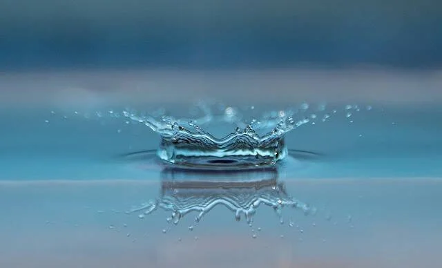 Macrofotografía de una gota de agua que forma una corona al impactar sobre una superficie líquida azul.