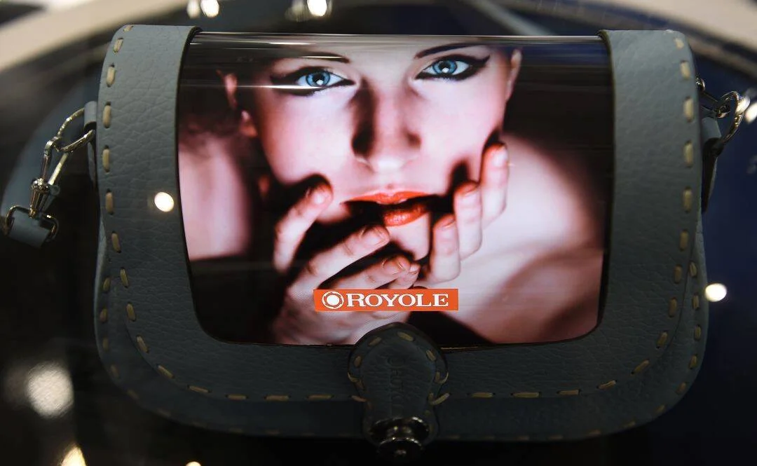Bolso de cuero con pantalla flexible de la marca Royole que muestra el rostro de una mujer con labios rojos.