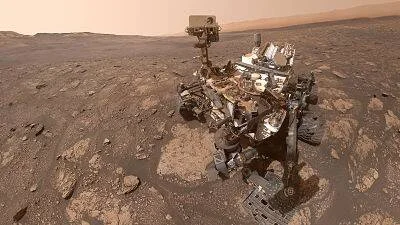 Róver de exploración sobre el suelo rocoso y rojizo de Marte bajo un cielo anaranjado.