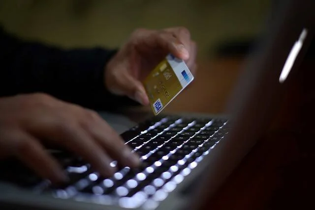 Manos de una persona sosteniendo una tarjeta de crédito dorada mientras escribe en la laptop para realizar un pago en línea.