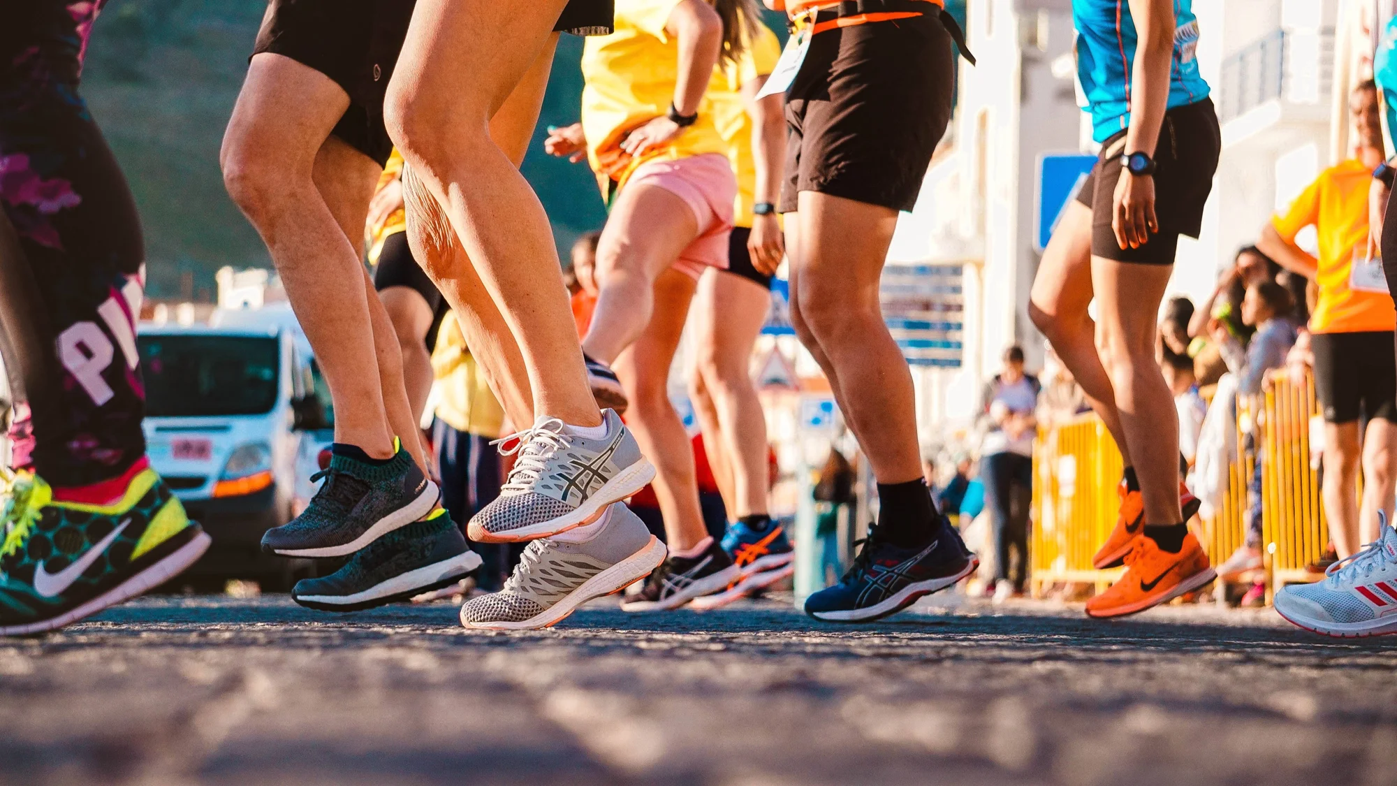 Grupo de corredores en una carrera urbana, captados desde las rodillas hacia abajo mientras corren con zapatillas deportivas de colores.