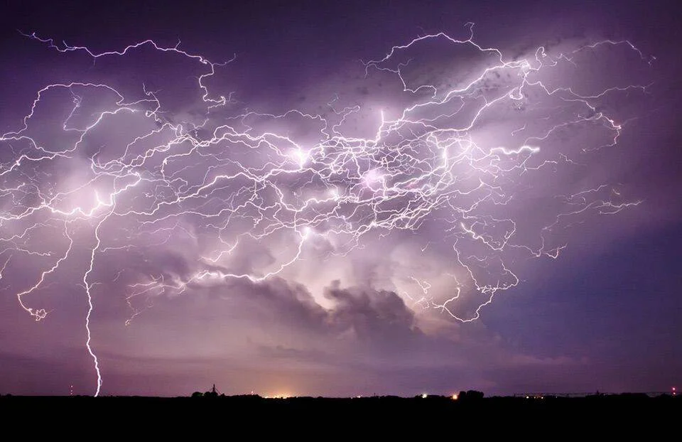 Múltiples rayos ramificados iluminan el cielo nocturno de color violeta sobre una línea de horizonte oscura.