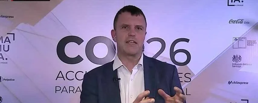 Hombre con traje azul habla frente a un telón del evento COP26 con logos de patrocinadores chilenos.