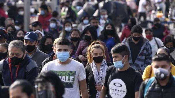 Numerosas personas caminan por una calle concurrida usando cubrebocas durante la pandemia.
