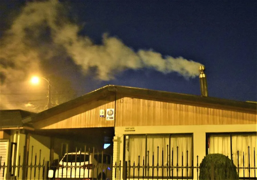 Chimenea de un edificio de madera expulsa una densa columna de humo blanco durante la noche.