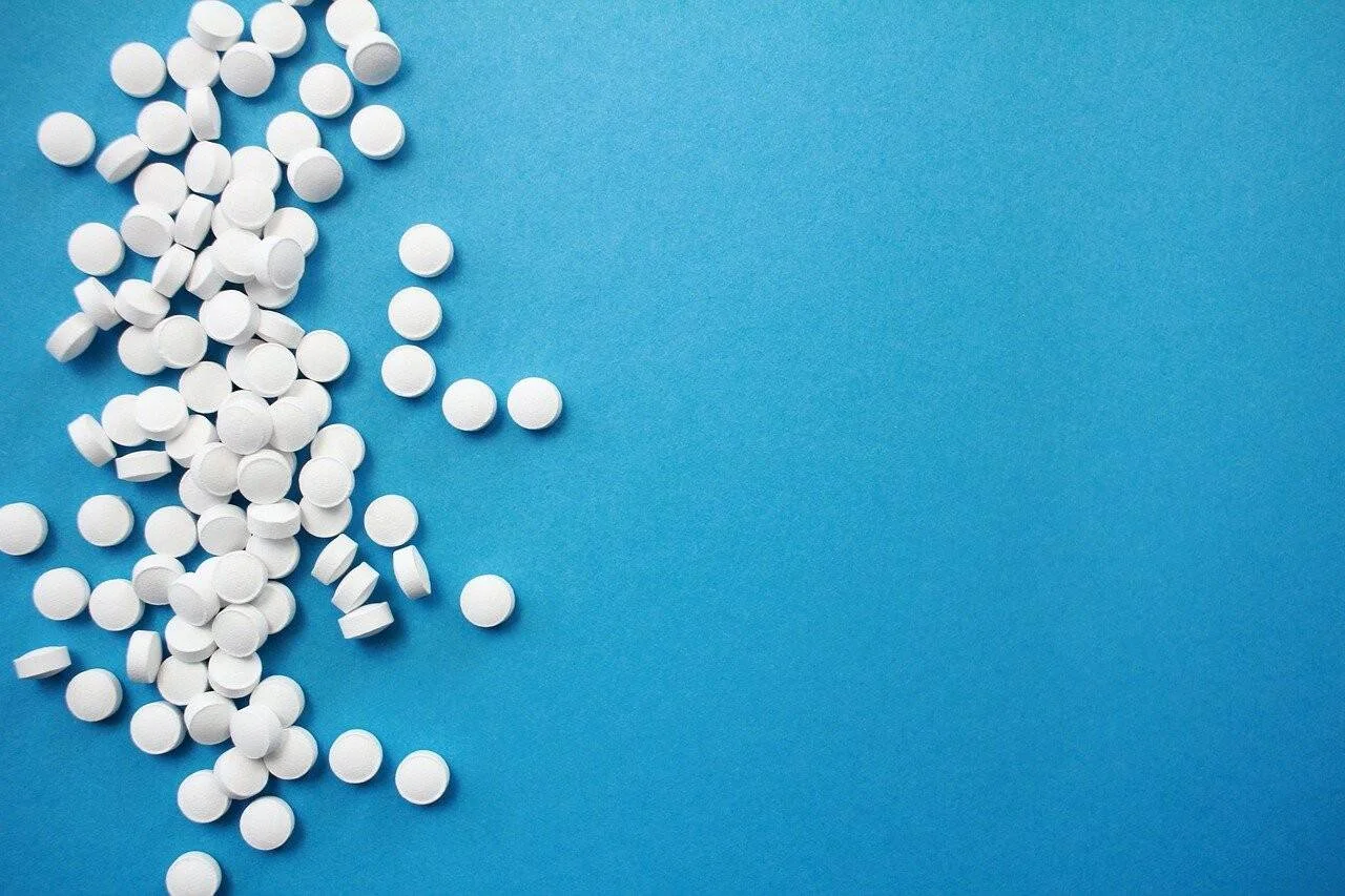 Numerosas pastillas redondas blancas esparcidas sobre una superficie azul.