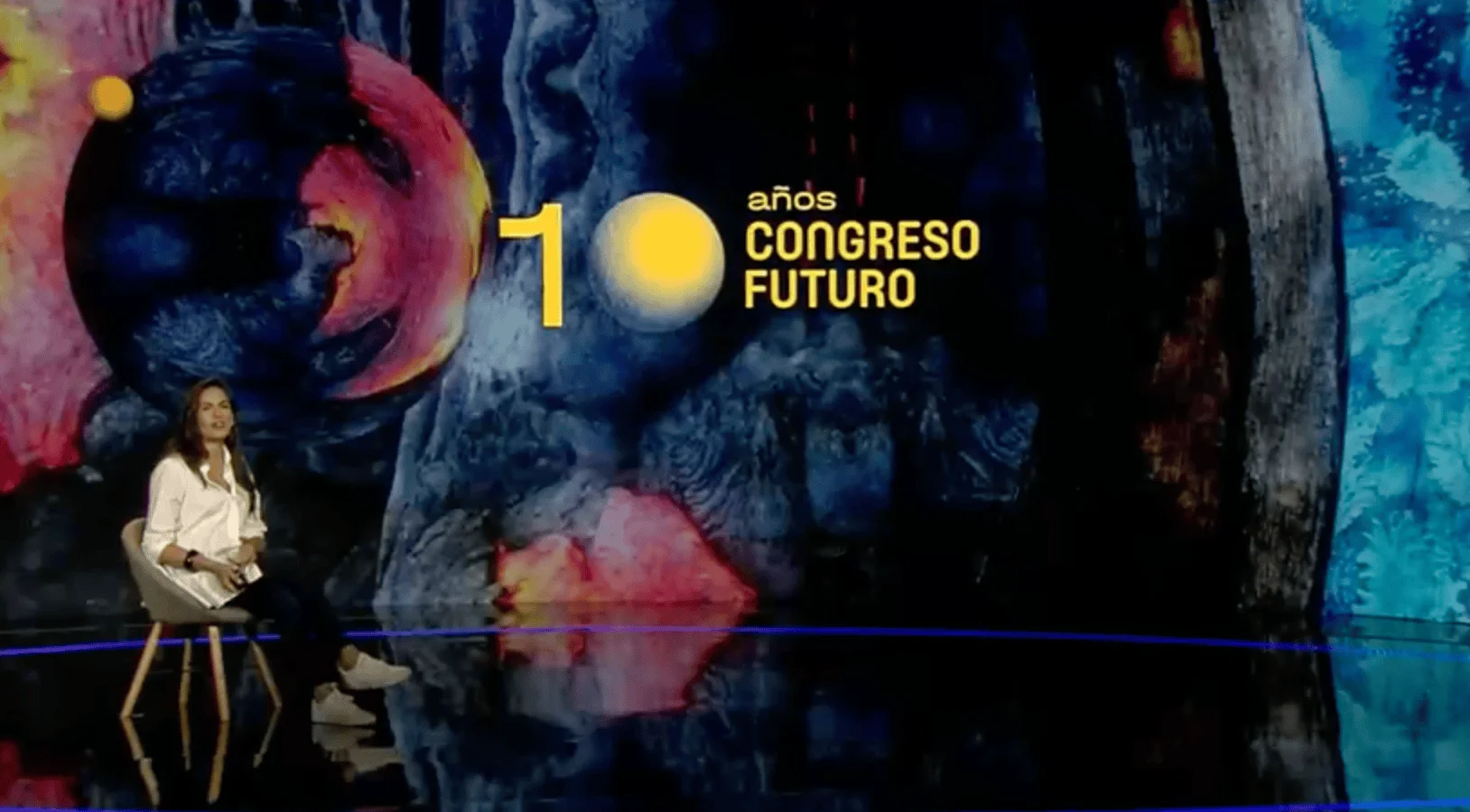Una mujer sentada en el escenario del Congreso Futuro, frente a una pantalla que celebra los 10 años del evento.