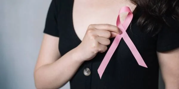 Mujer con remera negra sostiene un lazo rosa, símbolo de la concientización sobre el cáncer de mama.