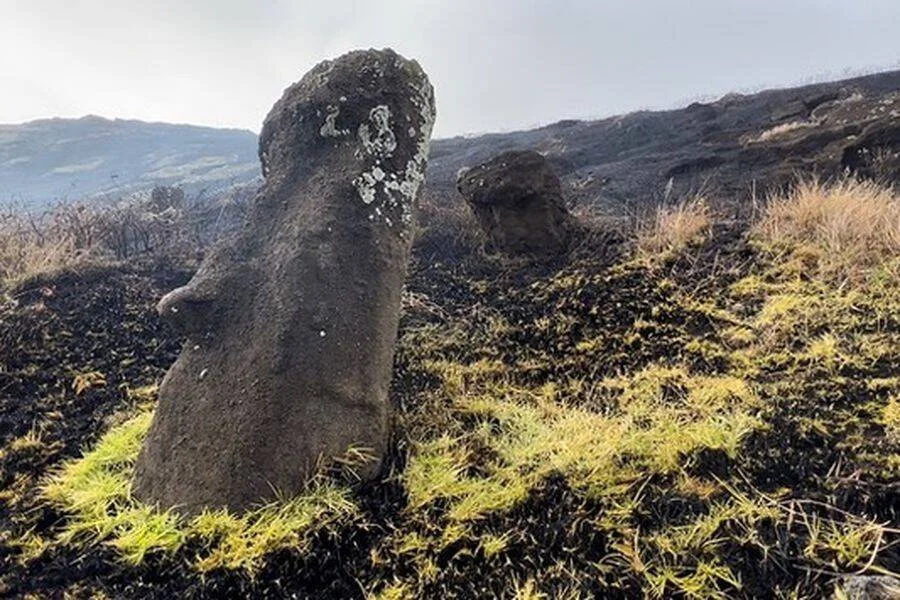 Dos estatuas moái rodeadas de vegetación quemada y suelo ennegrecido tras un incendio en Isla de Pascua.