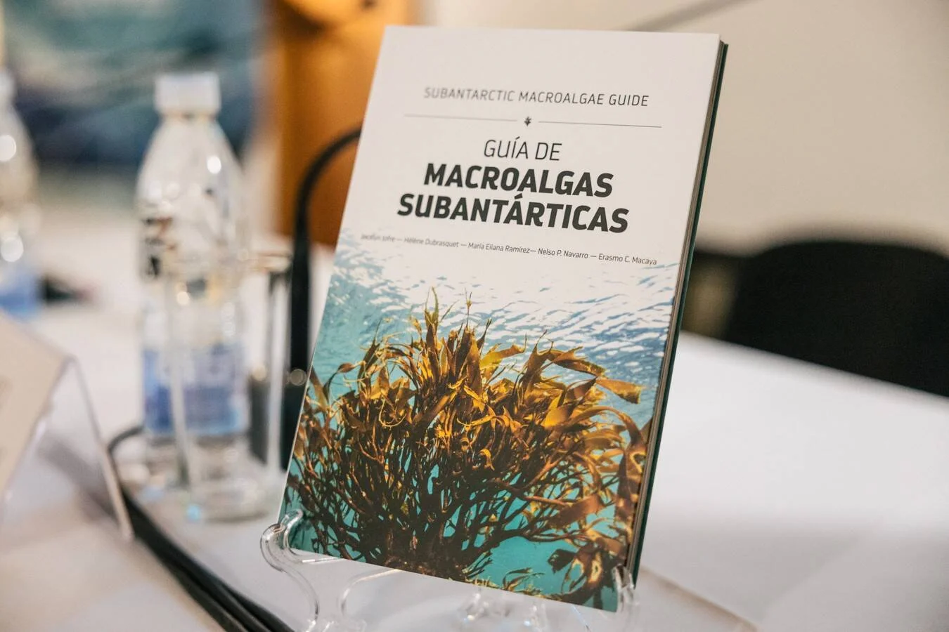 Ejemplar de la 'Guía de Macroalgas Subantárticas' exhibido en un atril sobre una mesa de reunión.
