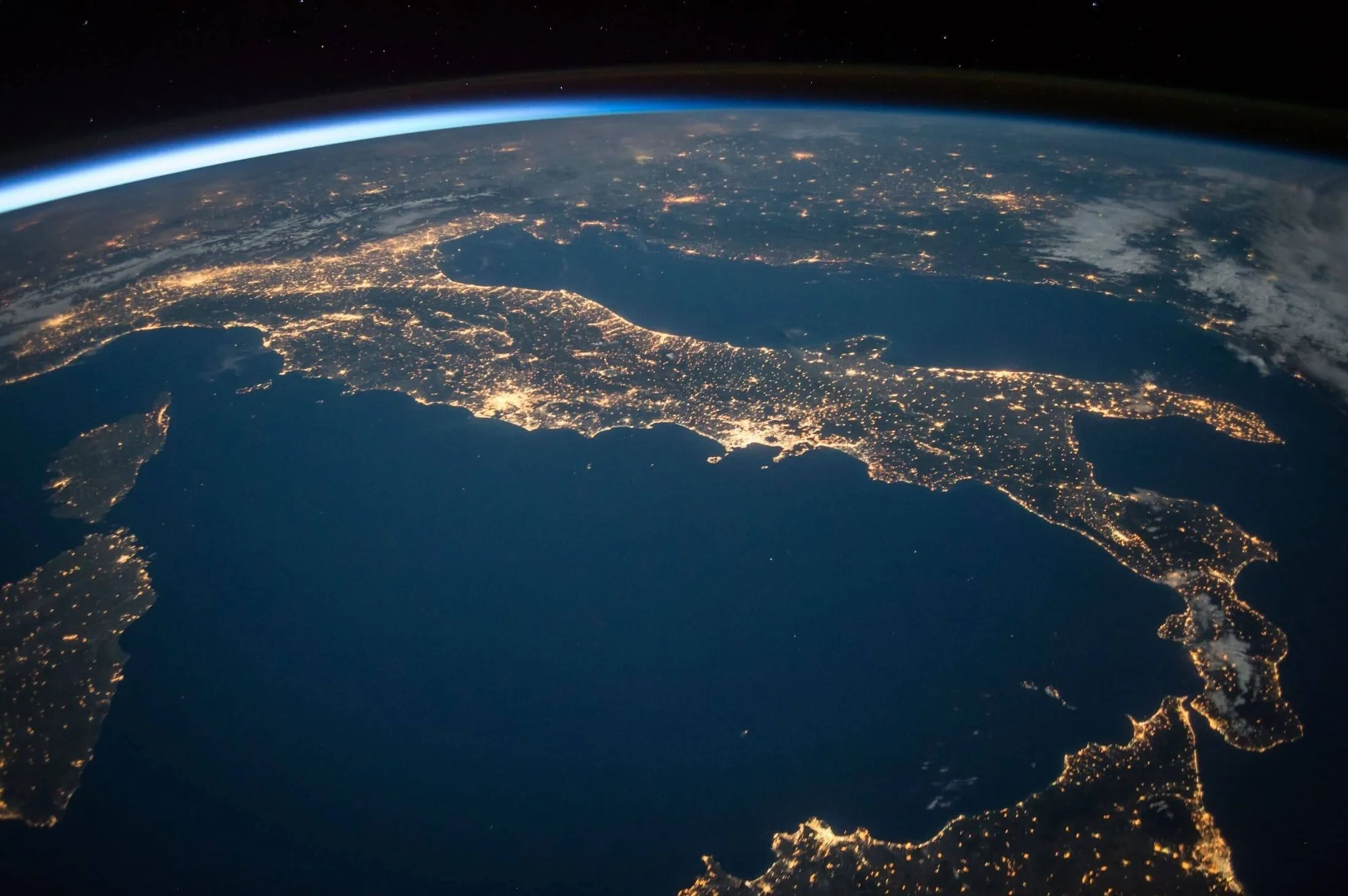 Vista nocturna de la península itálica desde el espacio, con las luces de las ciudades iluminando su contorno sobre el mar Mediterráneo.