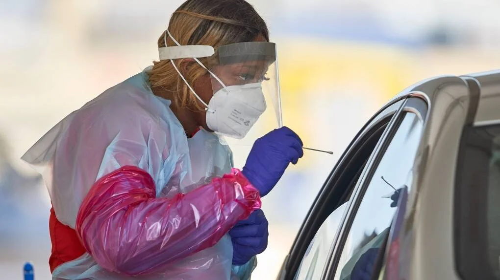 Profesional de salud con equipo de protección toma una muestra nasal con hisopo a una persona dentro de un vehículo.