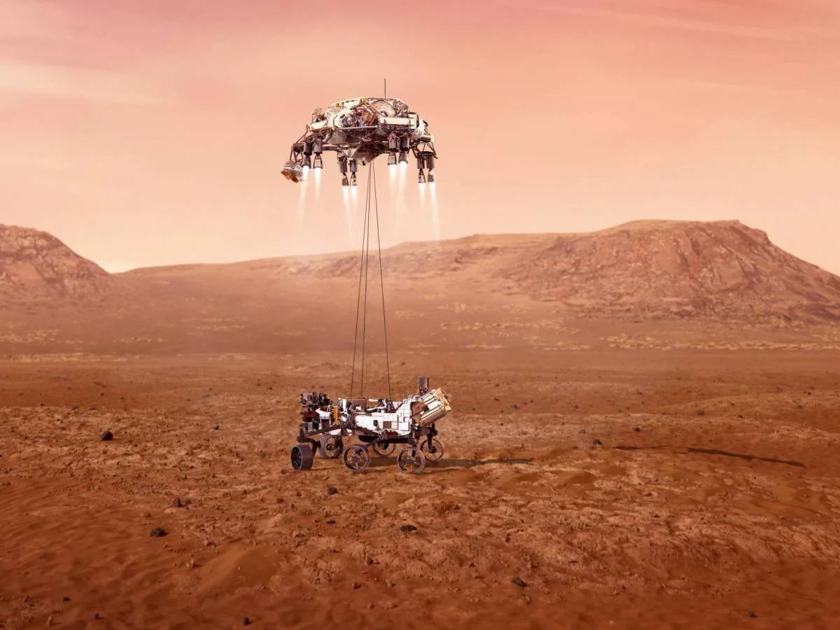 Ilustración de un róver espacial siendo descendido mediante cables desde una grúa aérea propulsada sobre la superficie rojiza de Marte.