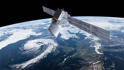 Satélite con paneles solares desplegados sobrevolando la Tierra, con nubes y continentes visibles de fondo.