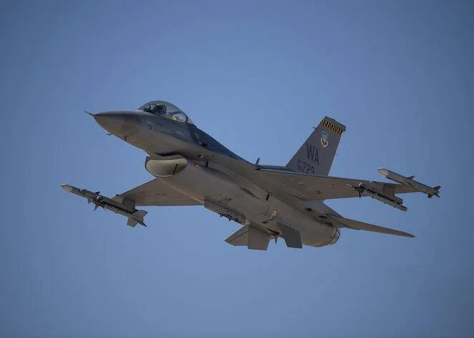 Avión de combate F-16 con marcas WA despegando armado con misiles bajo un cielo azul despejado.