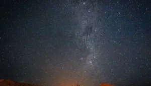 La Vía Láctea se extiende sobre un cielo estrellado con colinas rojizas en el horizonte bajo luz nocturna.