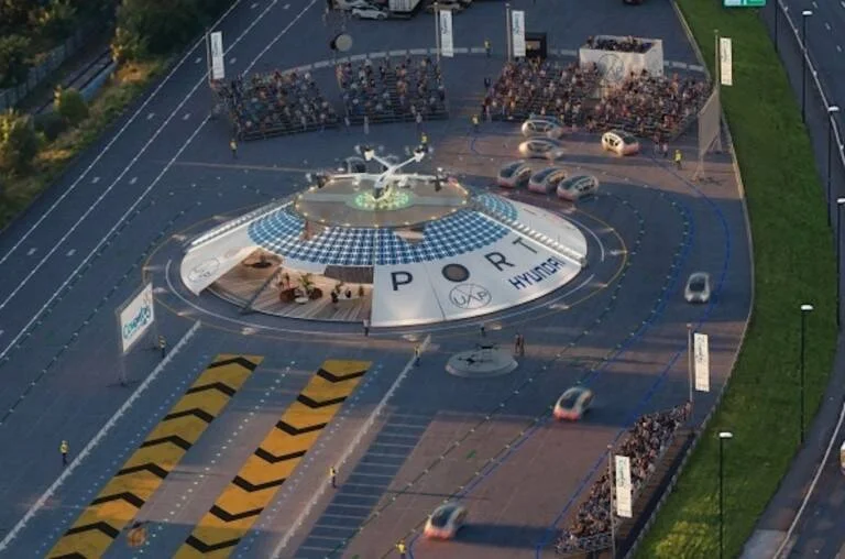 Render aéreo de un puerto urbano de movilidad avanzada con plataforma circular, vehículos autónomos y un taxi aéreo de Hyundai.