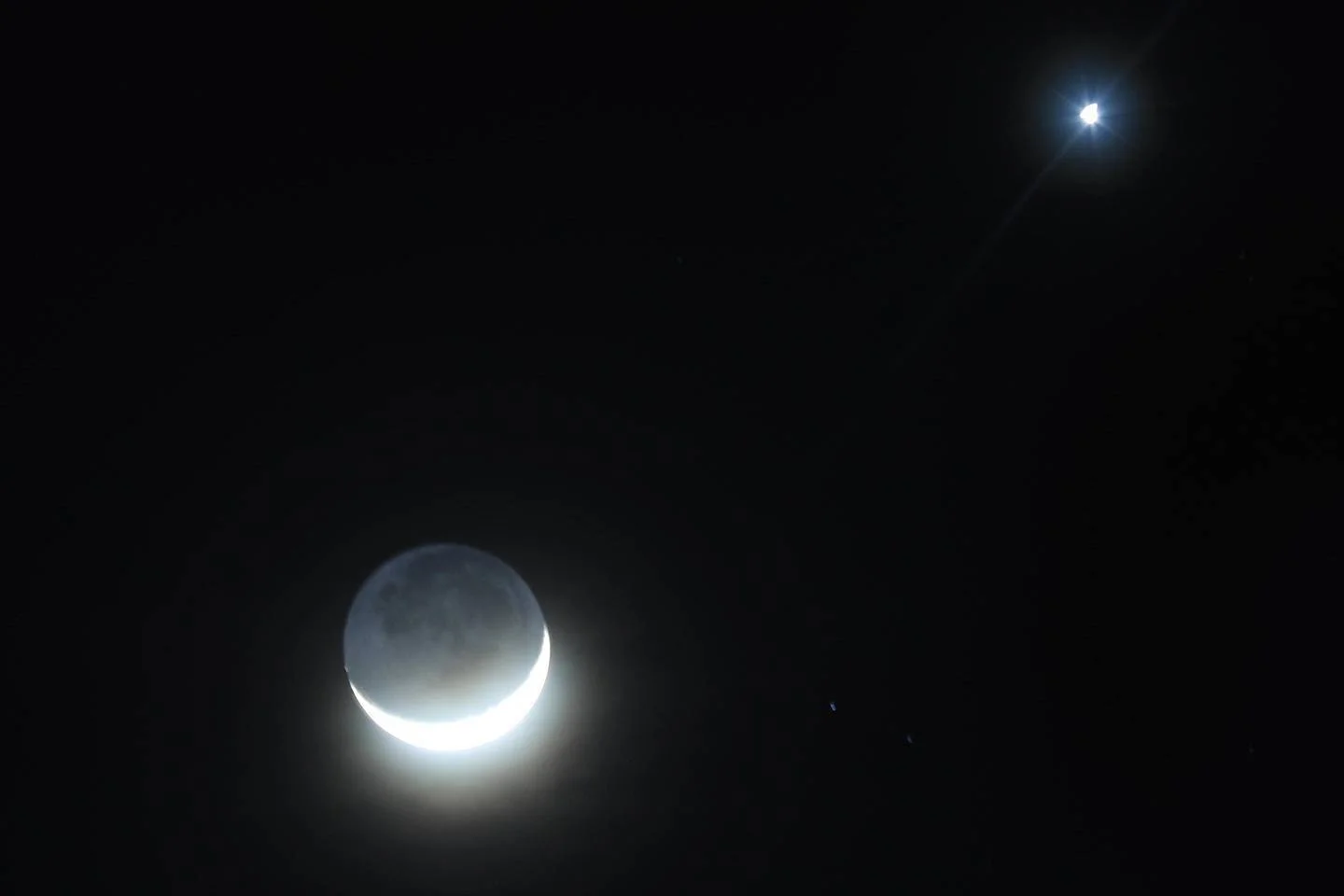 Luna en fase creciente con luz cinérea visible junto a un planeta brillante en el cielo nocturno oscuro.