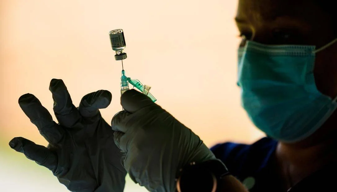 Un trabajador sanitario con guantes y mascarilla extrae una vacuna de un vial con una jeringa.