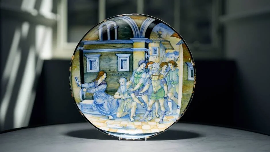 Plato antiguo de mayólica esmaltada con escena narrativa de figuras vestidas a la antigua, pintada en azul, verde y ocre.