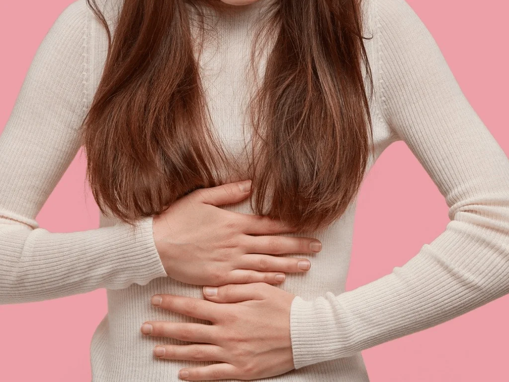 Mujer sujetándose el pecho con ambas manos, gesto que indica dolor o molestia en esa zona.