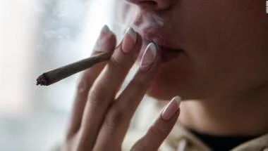 Primer plano de una persona sosteniendo y fumando un cigarrillo de cannabis.