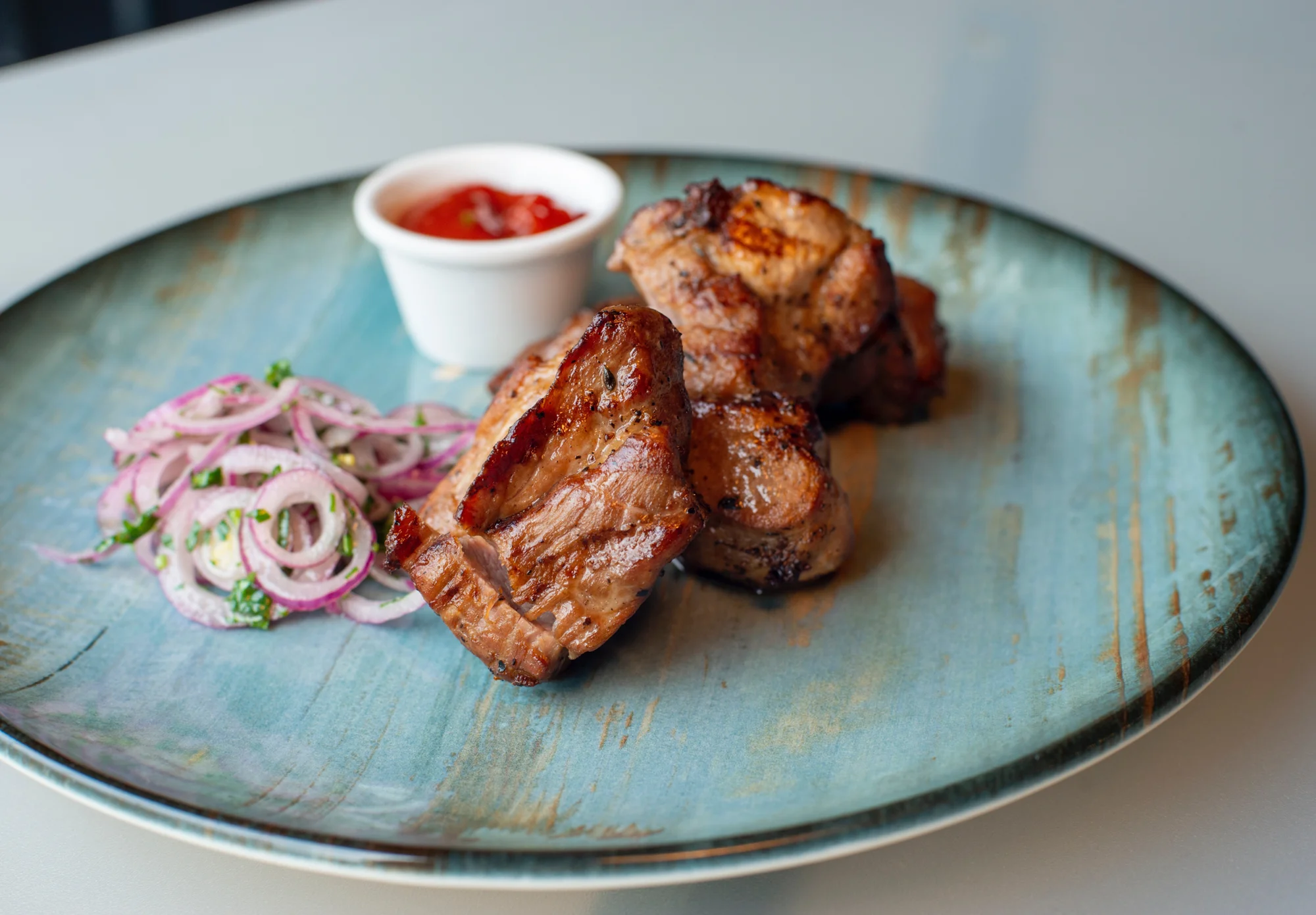Plato de carne asada a la parrilla acompañada de ensalada de cebolla morada y salsa roja, servida en plato turquesa.