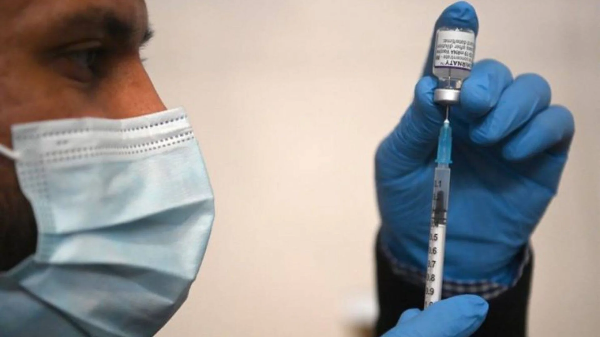 Profesional sanitario con mascarilla y guantes azules extrae dosis de una vacuna de ARNm en una jeringa.