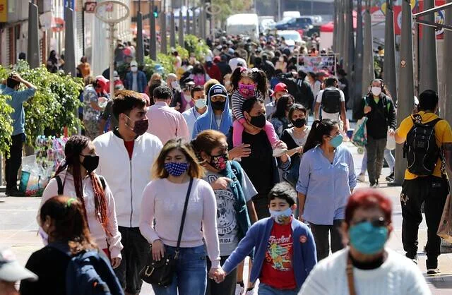 Gran cantidad de personas con mascarillas caminando por una concurrida acera urbana durante la pandemia.
