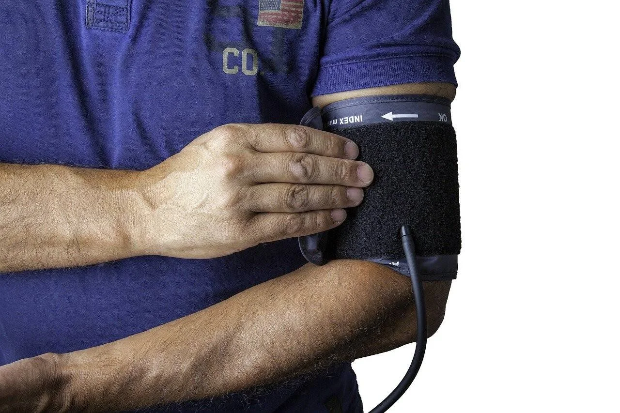 Hombre con camisa azul colocándose el manguito de un tensiómetro en el brazo para medir la presión arterial.