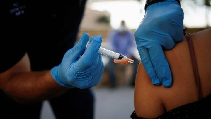 Un sanitario con guantes azules administra una inyección en el brazo de una persona.