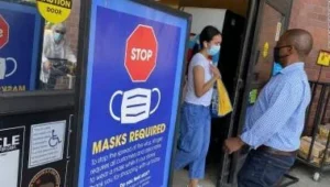 Personas con mascarilla junto a un cartel azul que exige el uso de cubrebocas en un establecimiento.