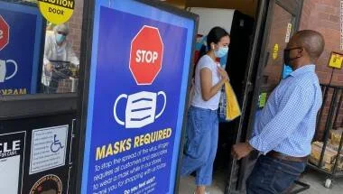 Personas con mascarilla junto a un cartel azul que exige el uso de cubrebocas en un establecimiento.