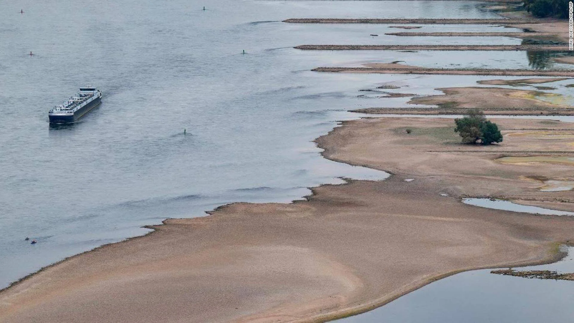 Vista aérea de un río con extensos bancos de arena expuestos por el bajo nivel del agua, con una barcaza navegando por el canal restante.