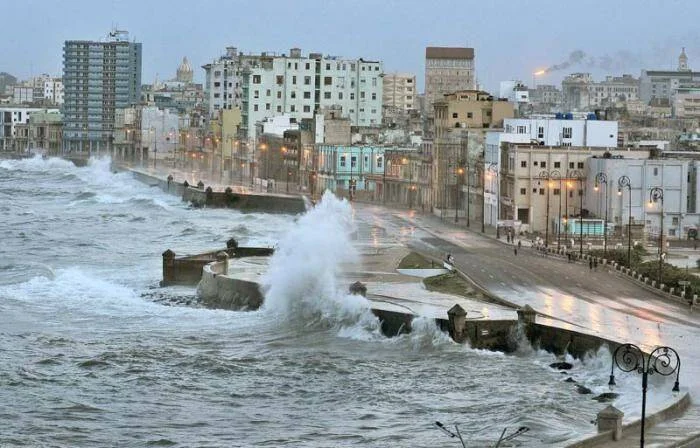 Fuertes olas rompen contra el Malecón de La Habana durante un temporal, con el paseo marítimo inundado y la ciudad al fondo.