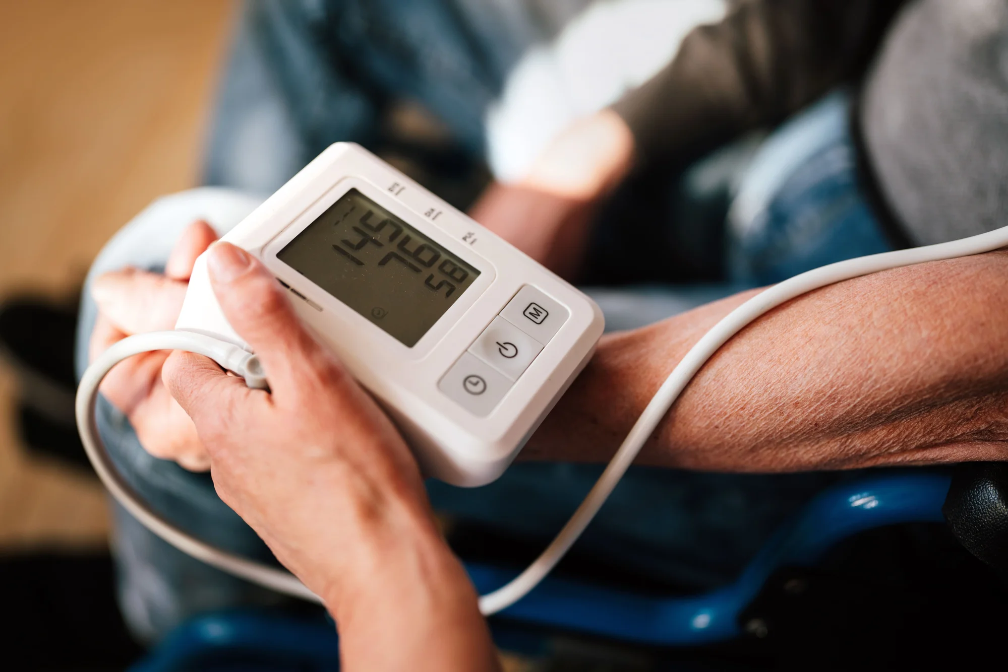 Una persona sostiene un tensiómetro digital mientras mide la presión arterial en el brazo de otra persona.