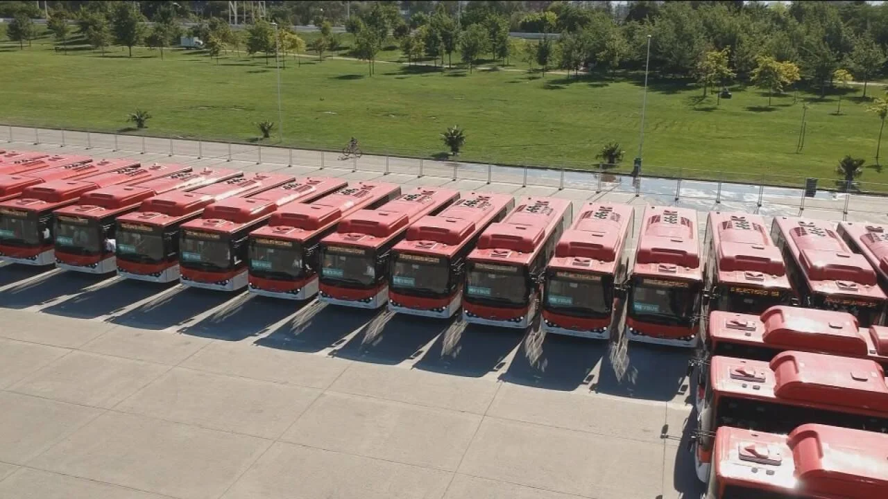 Decenas de buses rojos de transporte público alineados en un estacionamiento, vistos desde el aire.