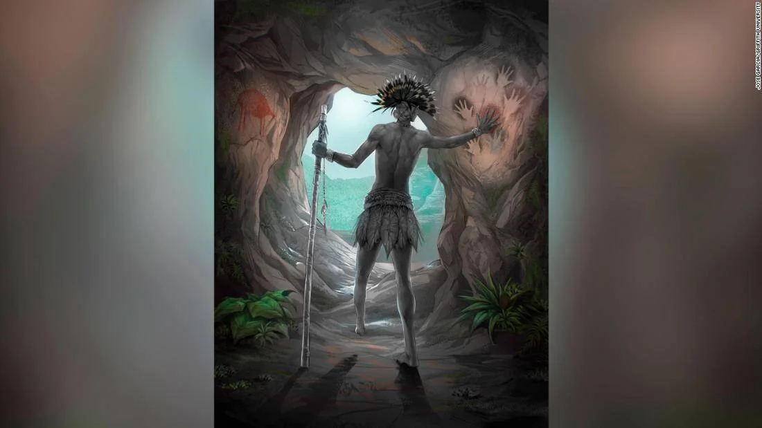 Ilustración de un hombre con tocado de plumas pintando siluetas de manos en las paredes de una cueva prehistórica.